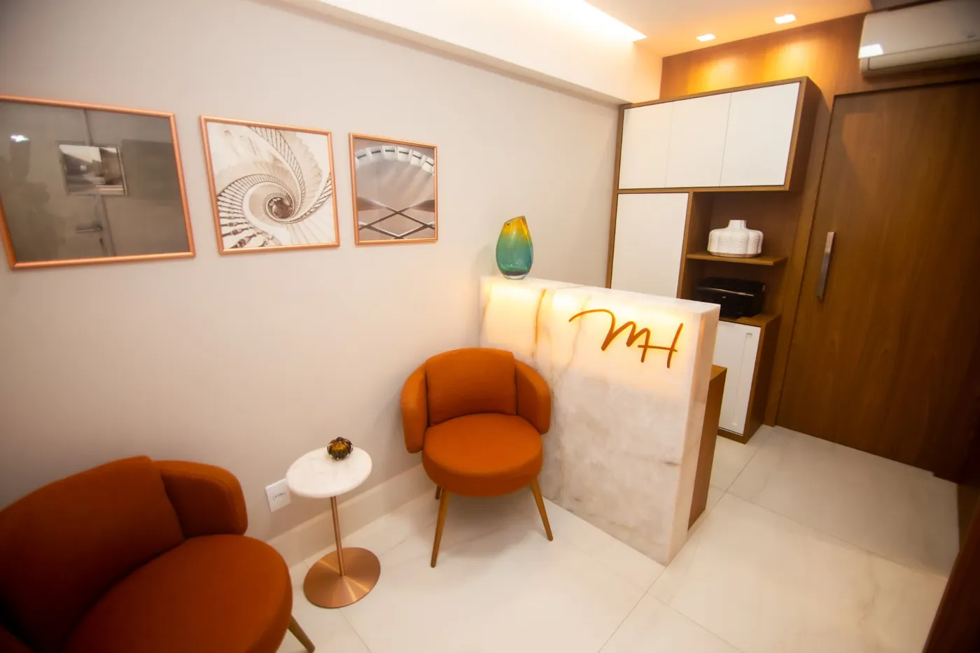 Recepção do consultório com poltronas terracota e balcão com o monograma MH